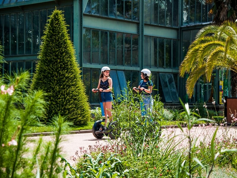 Tour en segway Lyon dans le parc de la Tête d’Or, deux femmes en gyropode profitent d’une balade au milieu des serres et de la végétation.