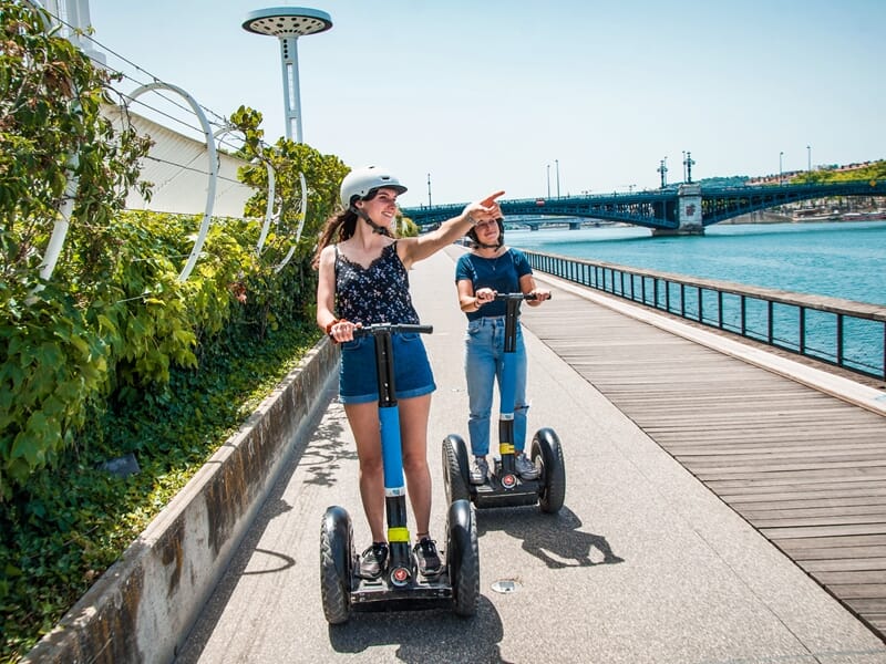Excursion en segway Lyon le long des quais du Rhône, deux participantes en gyropode admirent le paysage urbain et le fleuve.