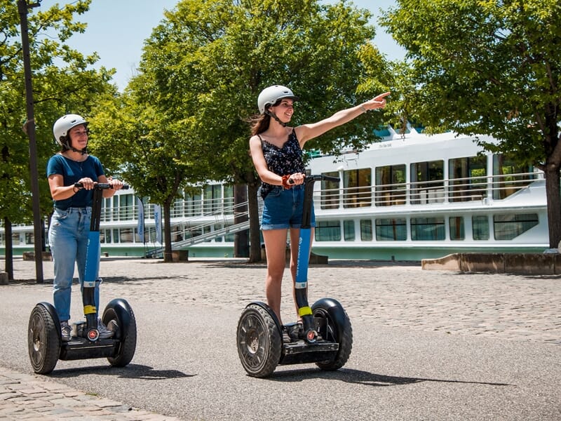 Tour en segway Lyon sur les berges de Saône, deux femmes en gyropode souriantes admirent les péniches et la ville.