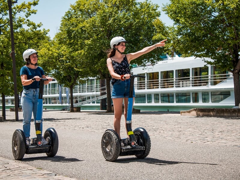 Tour en segway Lyon sur les berges de Saône, deux femmes en gyropode souriantes admirent les péniches et la ville.