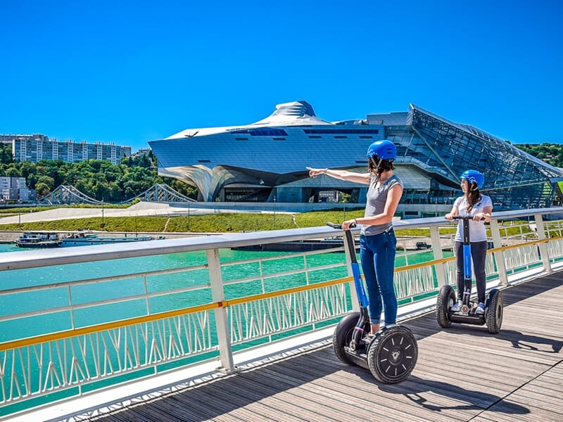 Balade en segway Lyon devant le musée des Confluences, deux participantes en gyropode admirent l’architecture moderne.