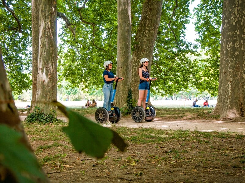 Promenade en segway Lyon dans le parc de la Tête d’Or, deux femmes en gyropode évoluent sous les grands arbres.