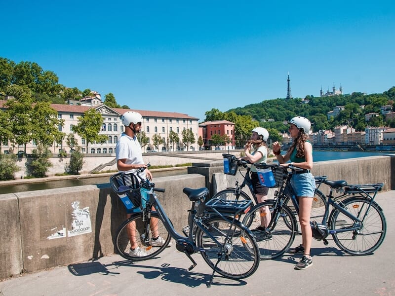 Groupe en balade vélo électrique Lyon au bord de la Saône, trois cyclistes en VAE s’arrêtent pour admirer le panorama sur Fourvière.