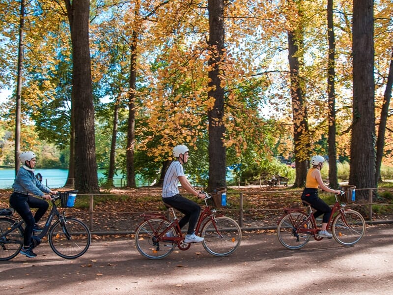 Balade vélo électrique Lyon au parc de la Tête d’Or en automne, trois cyclistes profitent d’une sortie parmi les arbres aux feuilles colorées.