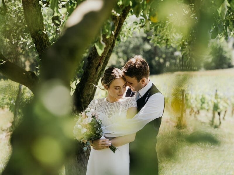 Couple de mariés enlacés tendrement sous un arbre, lors d'un shooting avec un photographe de couple à Amiens.