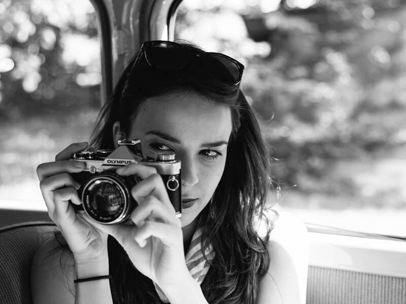 Jeune femme en noir et blanc tenant un appareil photo vintage lors d'un shooting photo lifestyle à Amiens.