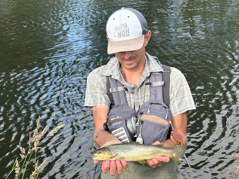 Jeune homme avec casquette tenant une truite dans ses mains lors d'un stage de pêche à Schirmeck.