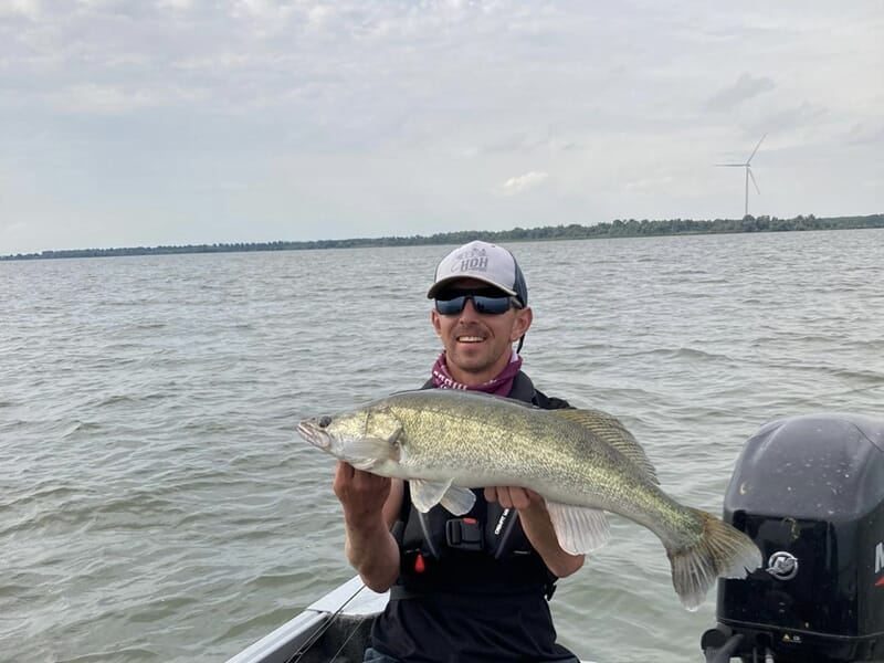 Homme souriant en bateau tenant un gros poisson pêché sur un lac lors d'un stage de pêche près de Strasbourg.
