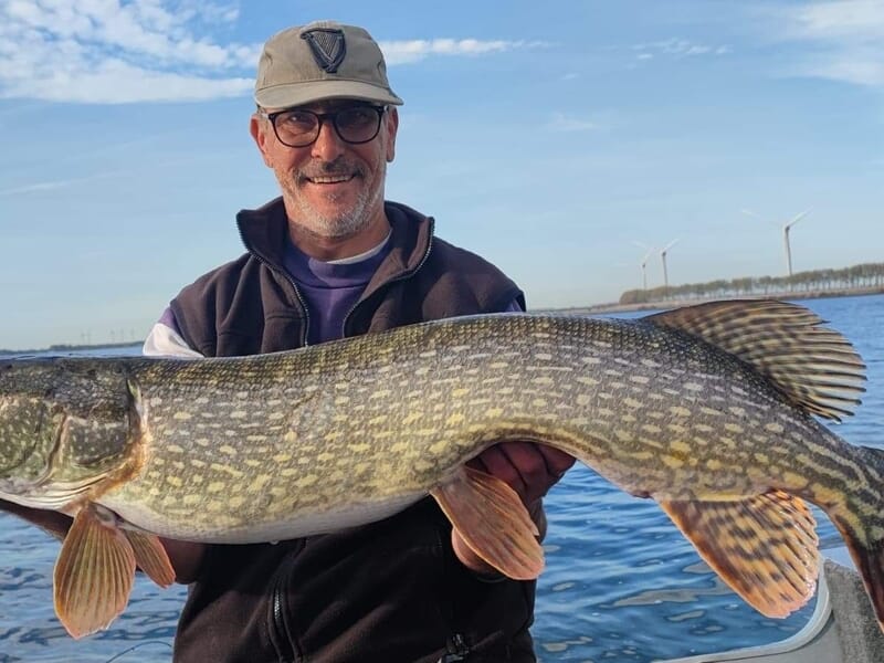Homme souriant tenant un grand brochet fraîchement pêché sur un bateau lors d'un stage de pêche près de Strasbourg.