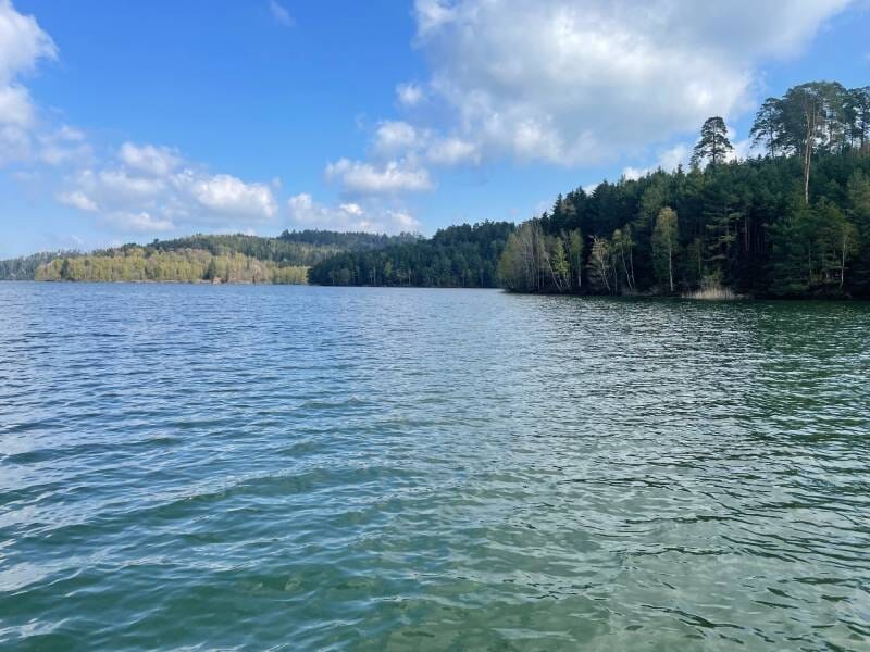 Paysage du lac de Pierre-Percée entouré de forêts verdoyantes sous un ciel partiellement nuageux.