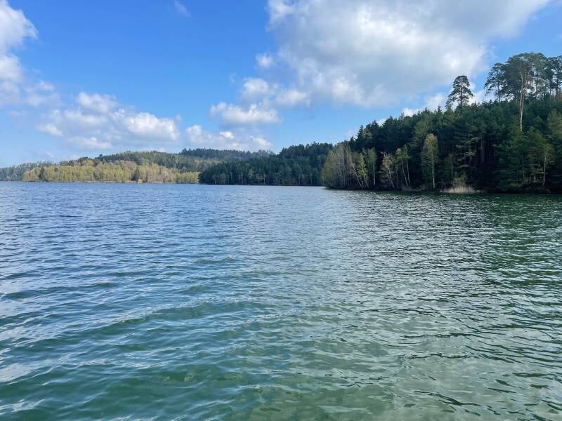 Paysage du lac de Pierre-Percée entouré de forêts verdoyantes sous un ciel partiellement nuageux.