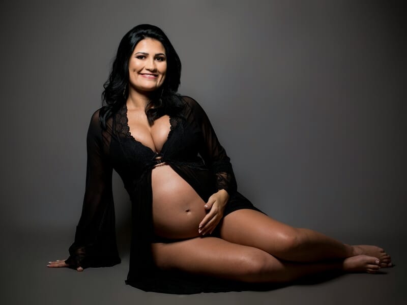 Femme enceinte souriante en robe noire transparente lors d'un shooting avec un photographe de grossesse près de Strasbourg.