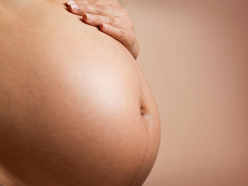 Gros plan sur un ventre de femme enceinte lors d'un shooting avec un photographe de grossesse près de Strasbourg.