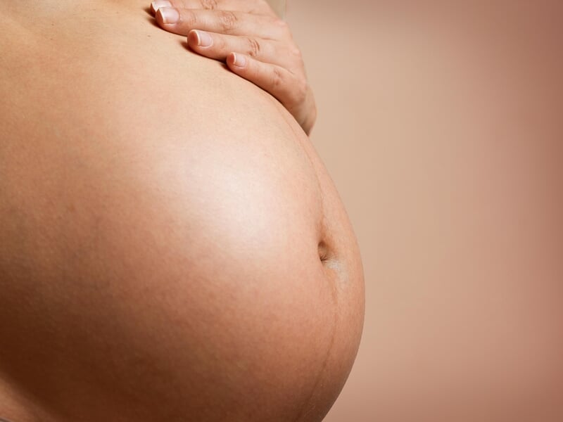 Gros plan sur un ventre de femme enceinte lors d'un shooting avec un photographe de grossesse près de Strasbourg.