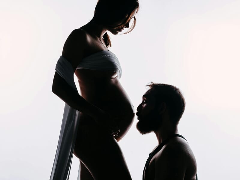 Homme embrassant le ventre d'une femme enceinte lors d'un shooting avec un photographe de grossesse près de Strasbourg.