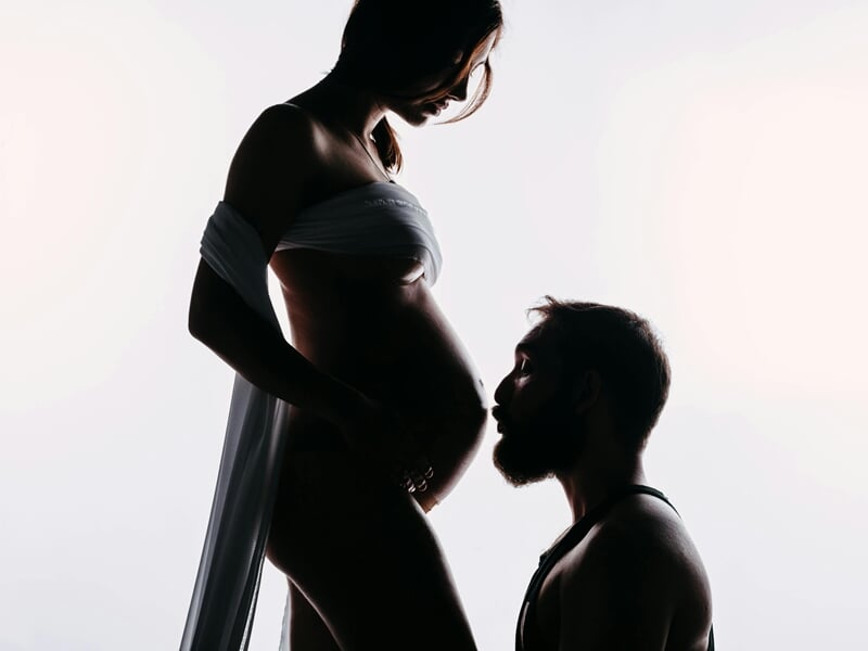 Homme embrassant le ventre d'une femme enceinte lors d'un shooting avec un photographe de grossesse près de Strasbourg.