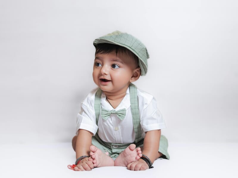 Bébé assis souriant portant un chapeau et un ensemble vert clair lors d'un shooting photo bébé près de Strasbourg.