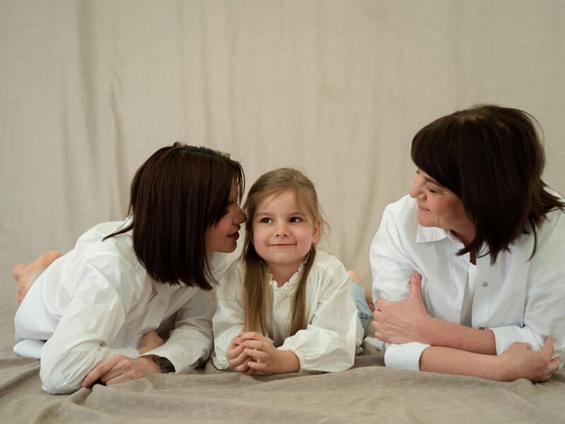 Deux mères et leur fille allongées sur un tapis lors d'un shooting avec un photographe famille.