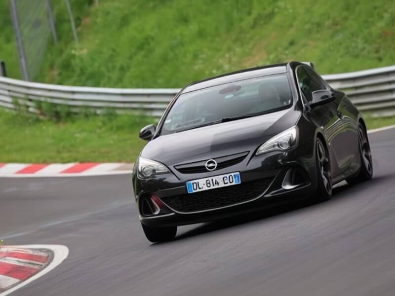 Opel Astra noire lancée à vive allure sur le circuit de Nürburgring, conduite dynamique sur piste.