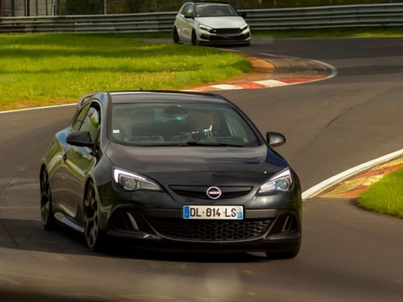Opel sportive noire suivie d’une autre voiture blanche dans un virage du circuit de Nürburgring.