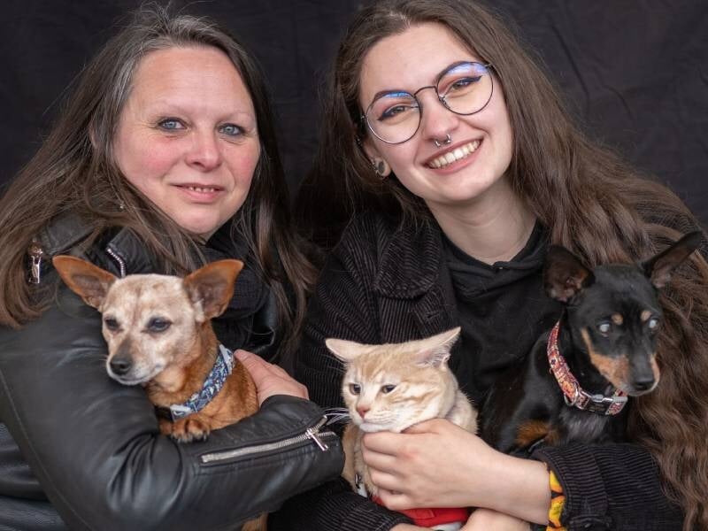 Deux femmes souriantes posent avec trois animaux : deux chiens et un chat, fond noir studio, à Nanterre.
