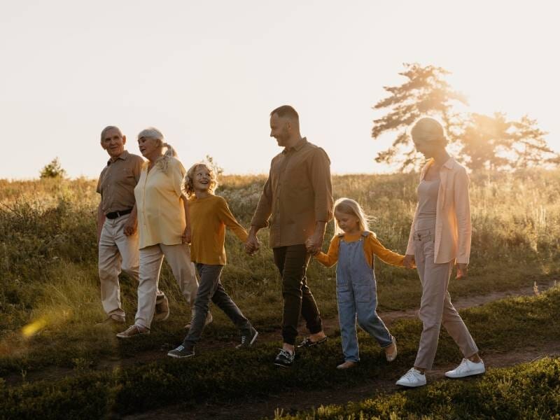 Une famille de plusieurs générations marchant main dans la main dans un champ au coucher du soleil.