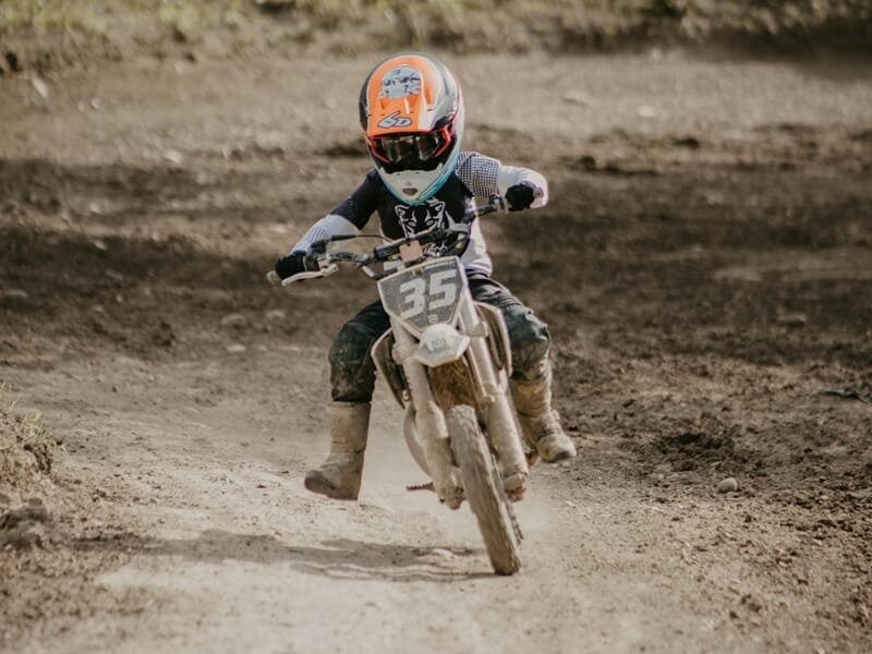 Un enfant en casque orange et tenue blanche conduit une moto tout-terrain lors d'un stage moto-cross enfant près de Nancy.
