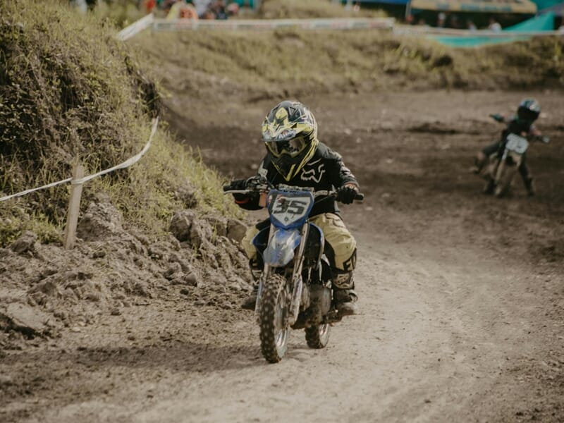 Un jeune pilote en tenue noire et jaune roule sur une moto tout-terrain lors d'un stage moto-cross enfant près de Nancy.