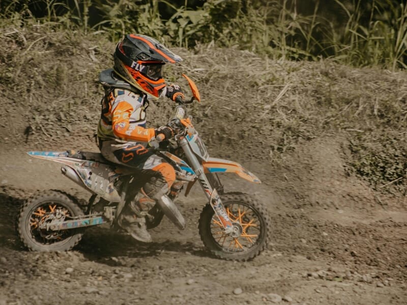 Un enfant en tenue orange et casque noir conduit une moto tout-terrain lors d'un stage moto-cross enfant près de Nancy.