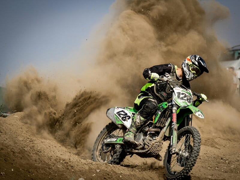 Motocross en action sur piste de terre, pilote en tenue noire et verte, lors d'un stage moto trail près de Nancy.