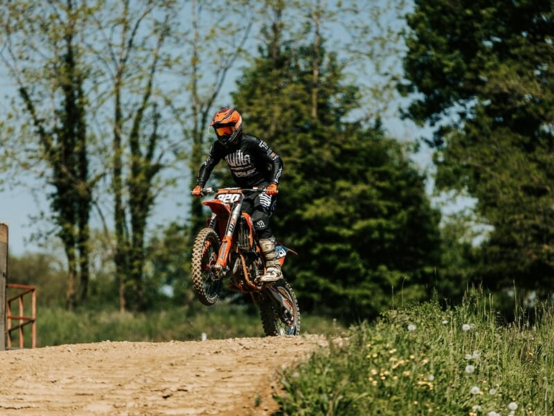 Pilote de moto tout-terrain en plein saut sur une piste de terre lors d'un stage moto trail près de Nancy.