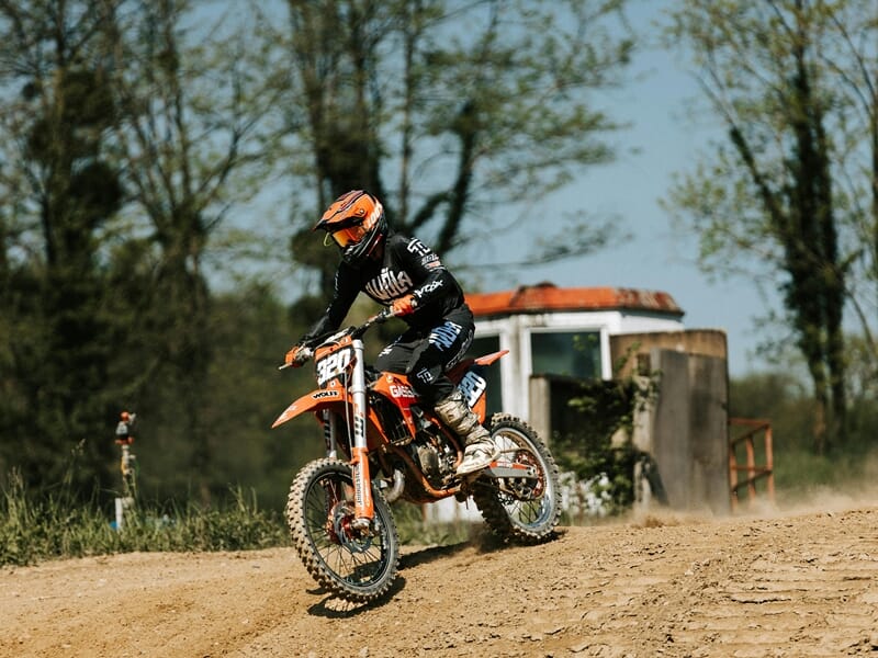 Motocross orange avec pilote en tenue noire et orange roulant sur une piste de terre lors d'un stage moto trail près de Nancy.
