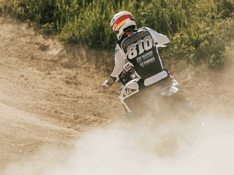 Pilote de moto tout-terrain en tenue blanche et noire sur piste poussiéreuse, lors d'un stage moto trail près de Nancy.