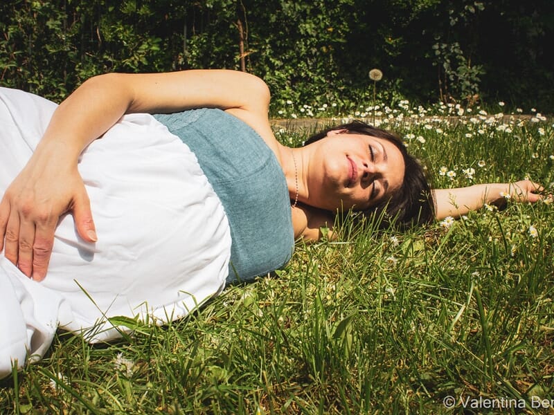 Femme enceinte allongée dans l'herbe au soleil lors d'un shooting avec une photographe grossesse à Béziers.