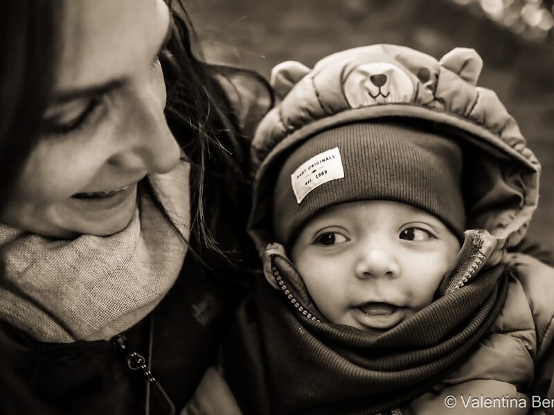 Une femme souriante regarde un bébé emmitouflé lors d'un shooting photo famille à Béziers.