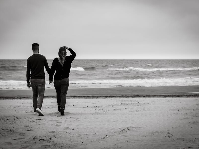 Un couple marche main dans la main sur une plage déserte lors d'un shooting avec une photographe de couple à Béziers.