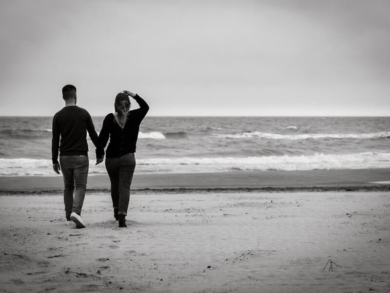 Un couple marche main dans la main sur une plage déserte lors d'un shooting avec une photographe de couple à Béziers.