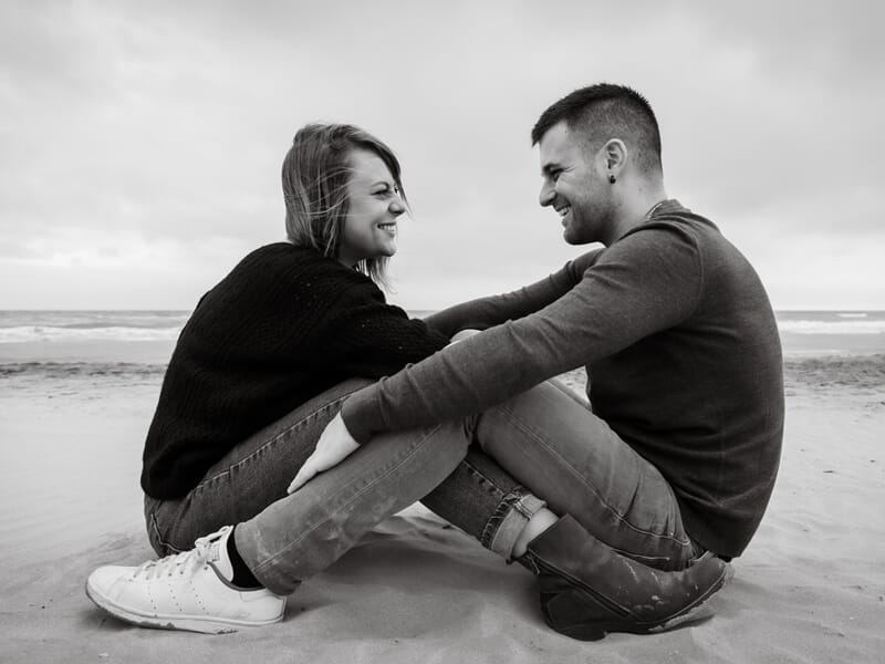 Un couple assis face à face sur le sable lors d'un shooting avec une photographe de couple à Béziers.