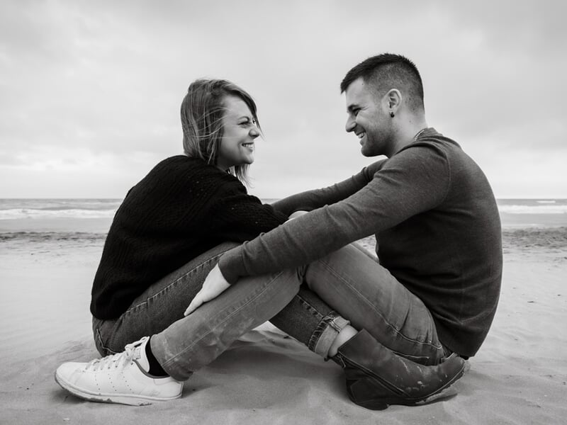 Un couple assis face à face sur le sable lors d'un shooting avec une photographe de couple à Béziers.