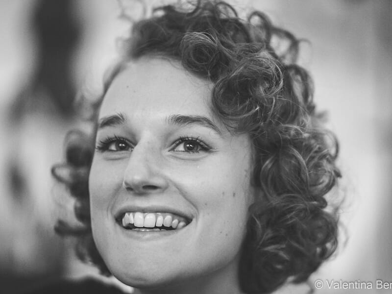 Portrait en noir et blanc d'une femme aux cheveux bouclés souriante lors d'un shooting photo portrait à Béziers.
