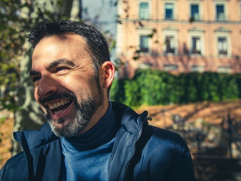 Homme souriant avec barbe et veste noire lors d'un shooting avec une photographe lifestyle à Béziers.