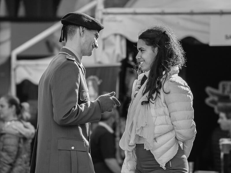 Un homme en uniforme militaire parle avec une femme souriante, photo prise lors d'un stage photo à Béziers.