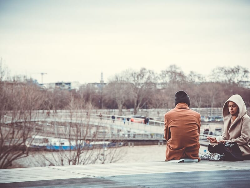 Deux personnes assises dos à dos sur un banc en bois près d'une rivière, photo prise lors d'un stage photo à Béziers.