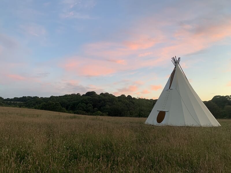 Tipi blanc installé dans un champ au coucher du soleil lors d'un stage de survie à Le Saint.