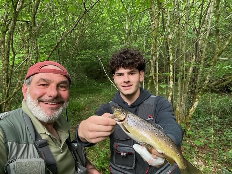 Deux hommes souriants en forêt, l'un tenant une truite fraîchement pêchée lors d'un stage de pêche près de Limoges.
