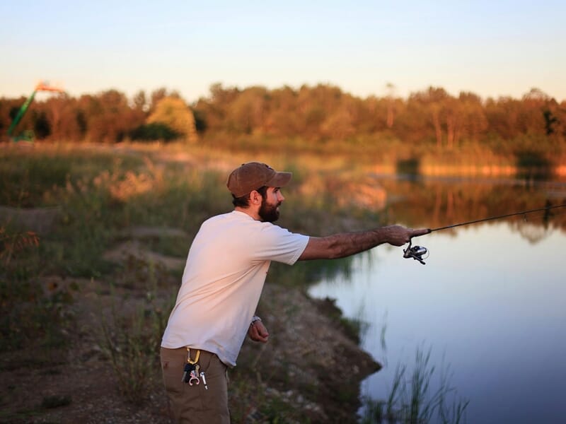 Homme barbu lançant sa ligne de pêche dans un étang calme au coucher du soleil lors d'un stage de pêche près d'Agen.
