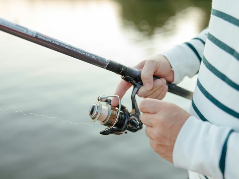 Mains d'une personne en pull rayé manipulant une canne à pêche lors d'un stage de pêche près d'Agen.