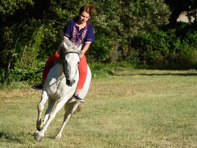 Jeune femme en tenue décontractée montant un cheval blanc au galop lors d'un shooting photo lifestyle à Nîmes.