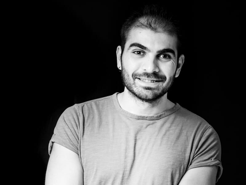 Portrait en noir et blanc d'un homme souriant, bras croisés, sur fond noir lors d'un shooting photo portrait à Nîmes.