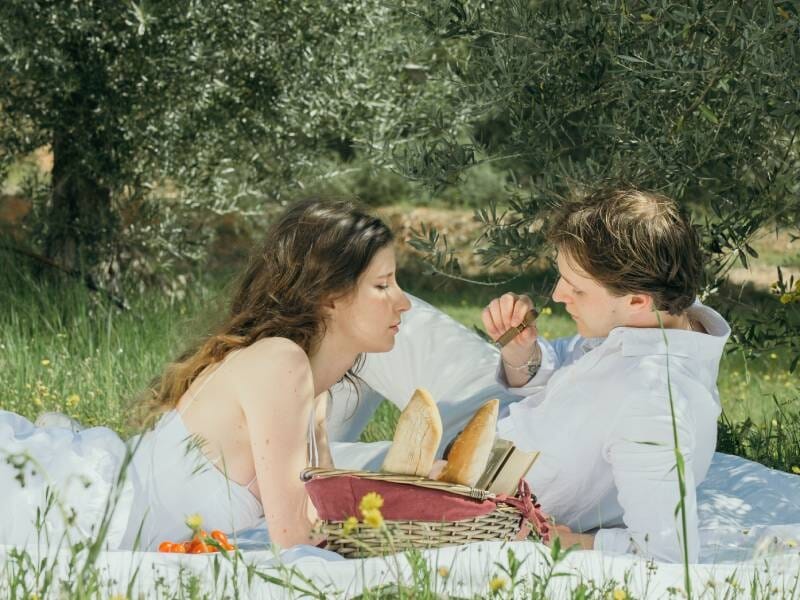 Un couple partageant un moment tendre près d'un panier de pique-nique avec du pain, dans un champ verdoyant, lors d'une séance photo à Aix-en-Provence.